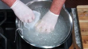 A Person Wearing Gloves Rinsing Freshly Made Butter in A Bowl of Ice Water