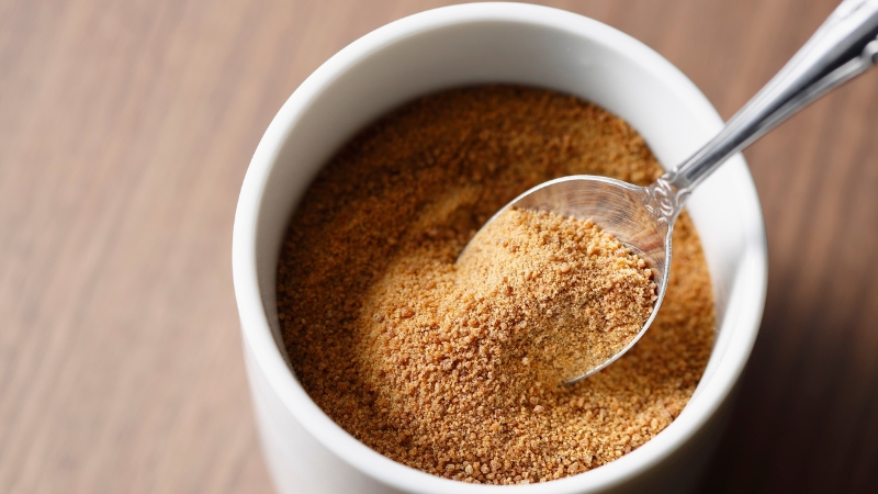 Spoon scooping maple sugar from a white bowl, showing its fine texture and rich brown color
